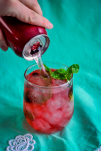 Club soda being poured into a glass of haskap mojito with muddled haskap berries and fresh mint.