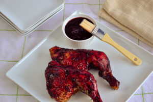 Close-up of a glazed chicken leg with a side ramekin filled with haskap BBQ sauce.