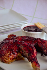 Elegantly plated grilled chicken leg glazed with haskap BBQ sauce, with a white ramekin of sauce on a clean white background.