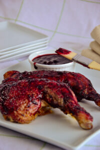 Grilled chicken leg coated in haskap BBQ sauce with a ramekin of extra sauce in the background.
